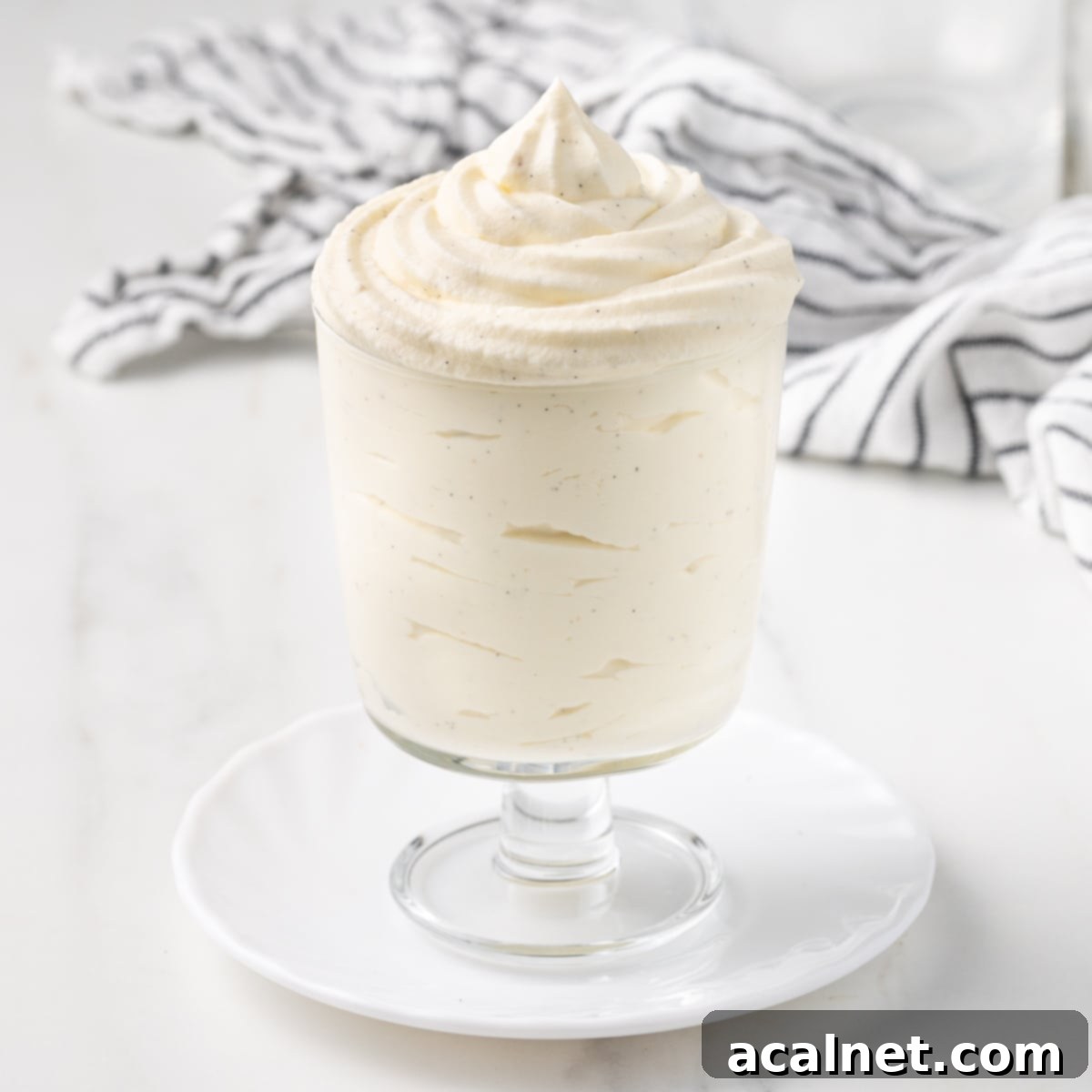 Cream piped inside a glass cup over a small white plate with a striped tea towel in the background, showcasing the beautiful texture of Chantilly Cream.