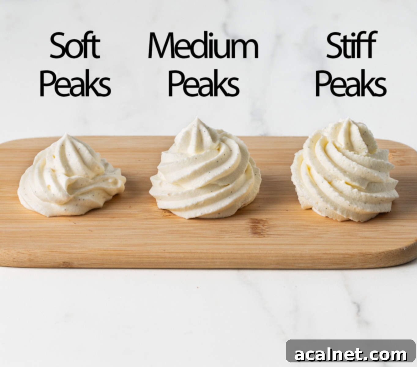 Dollops of chantilly cream at different whipping stages, piped over a small wooden board to illustrate soft, medium, and stiff peaks.