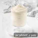 Cream piped inside a glass cup over a small white plate with a striped tea towel in the background.