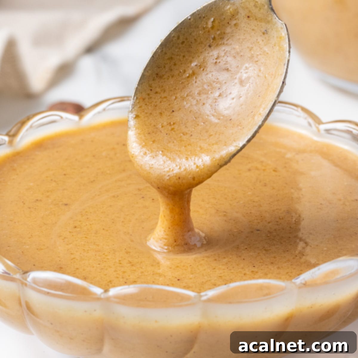 Close up on the hazelnut praline paste dripping from a spoon inside a glass bowl, showcasing its smooth and rich texture.