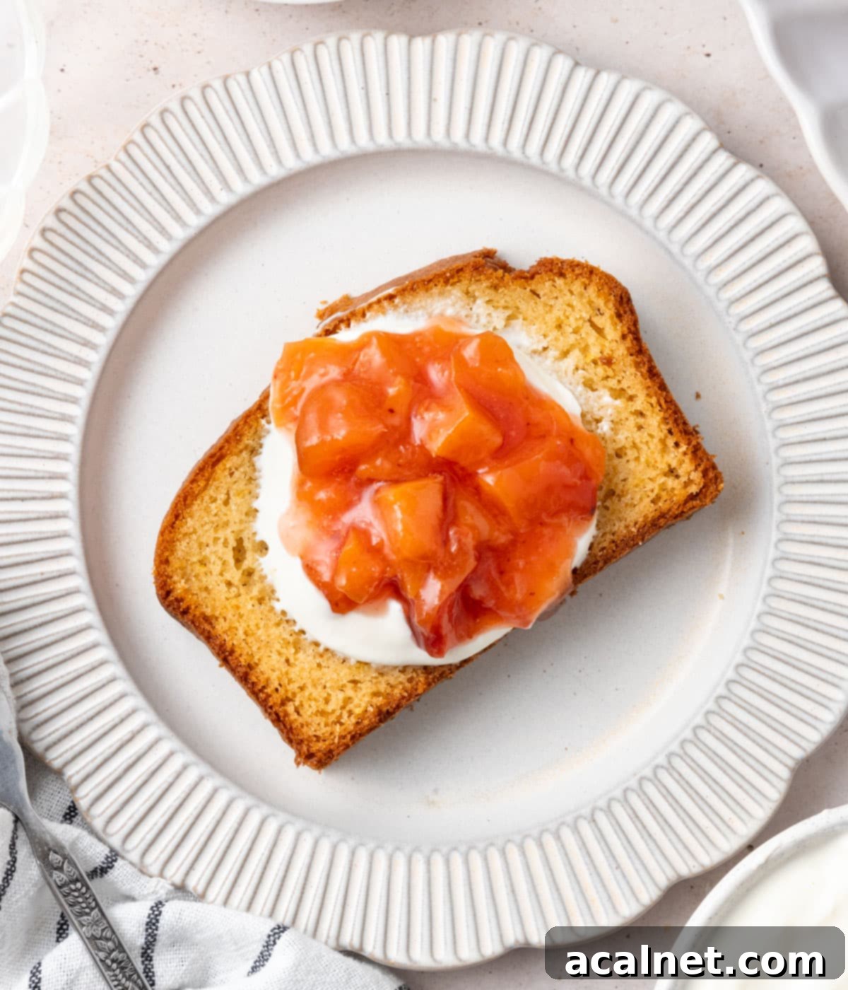A slice of cake topped with yogurt and peach compote seen from above on a small white plate.