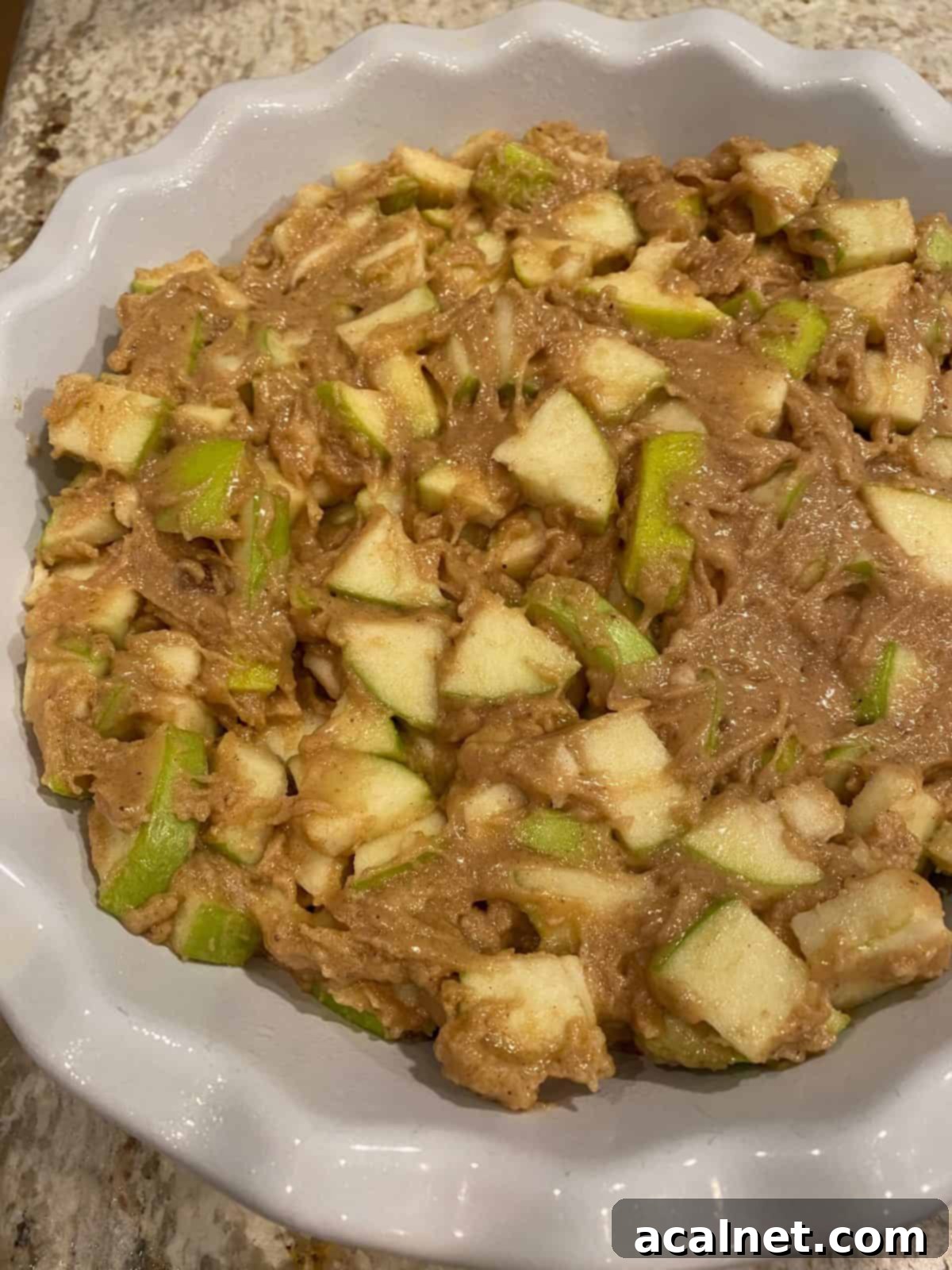 Unbaked apples with cake batter in a pie dish.