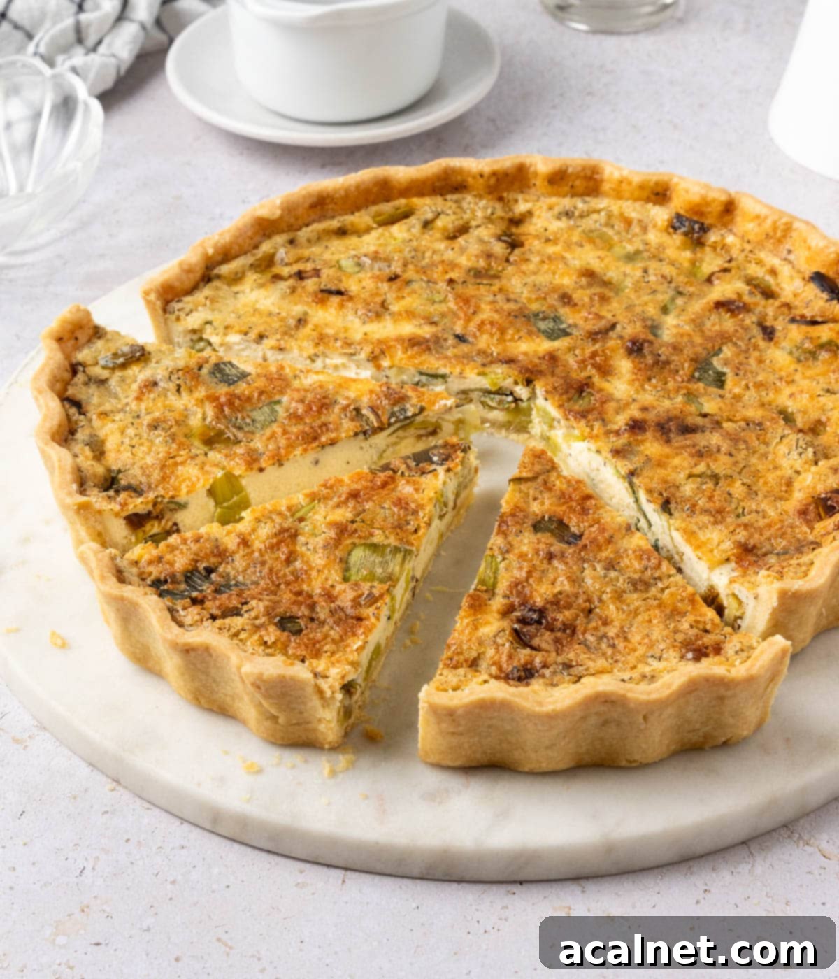 45 degrees angle view on the quiche with three slices cut out, showing the layers of leek and creamy cheese.