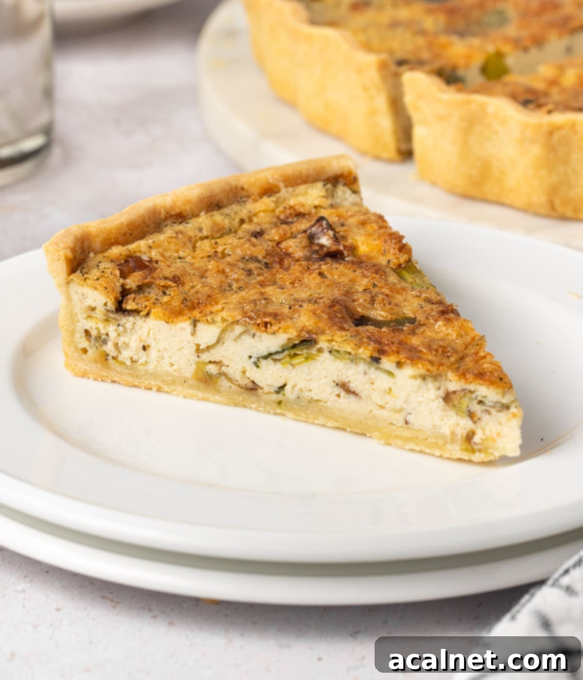 One slice of quiche on a small white plate, showing the flaky crust and creamy filling.