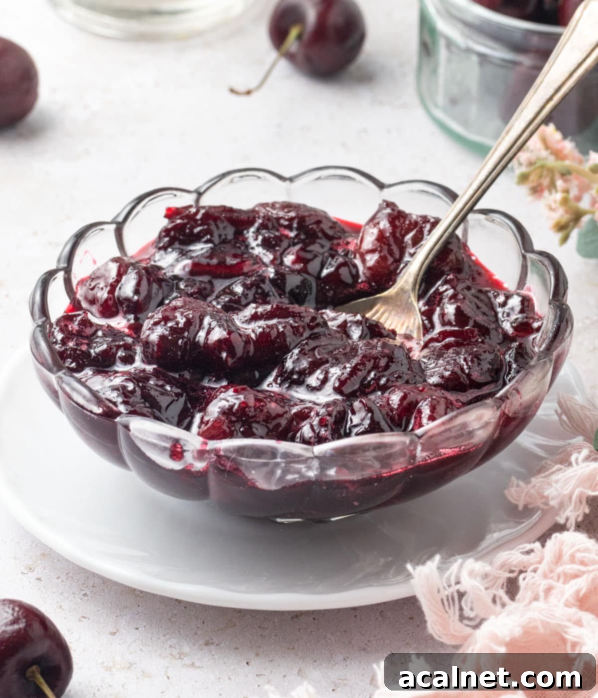 Sauce in a glass cup placed on a small white plate with a silver spoon.