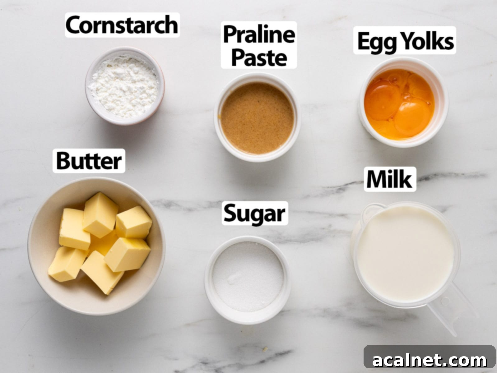 Velvety Praline Mousseline 3 Ingredients for praline mousseline cream laid out on a marble surface, including milk, eggs, sugar, cornstarch, butter, and praline paste.
