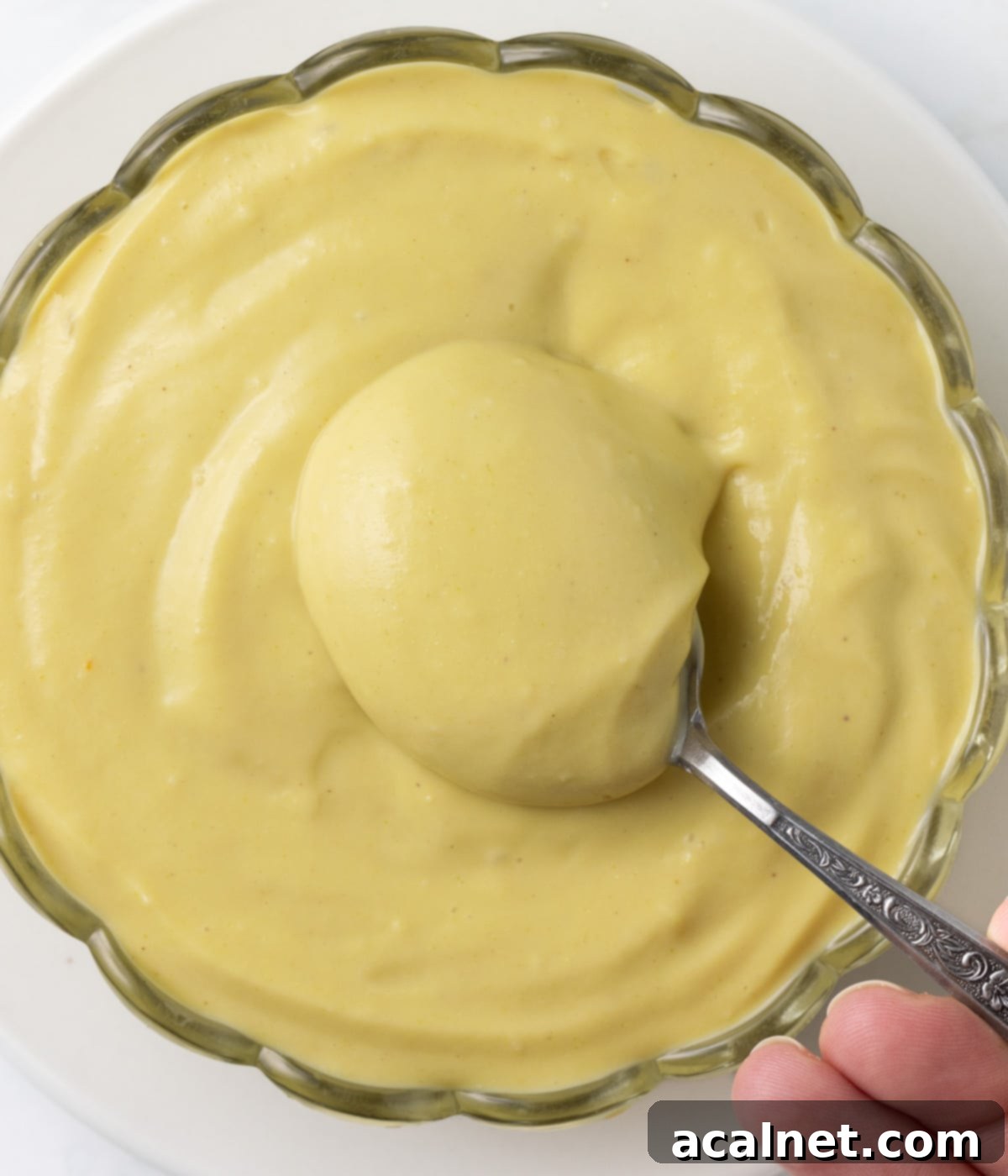 Picking up cream from a glass bowl with a spoon seen from above.