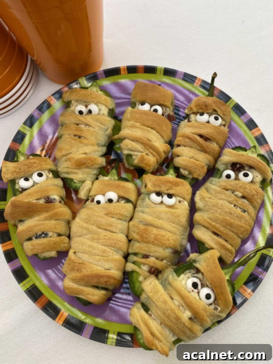 A plate with eight wrapped jalapeño bacon mummies wrapped in dough, garnished with candy eyes.