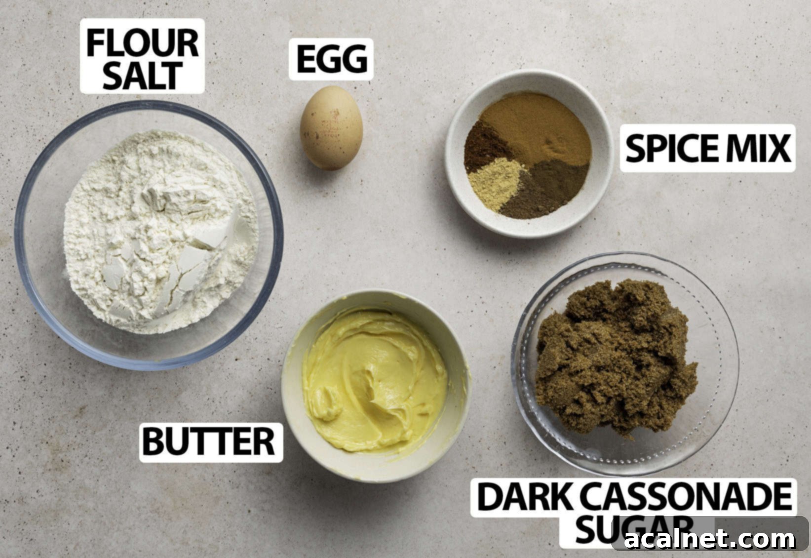 A selection of Speculoos ingredients, including flour, sugar, butter, and spices, neatly arranged on a light beige surface for a clear overhead view.