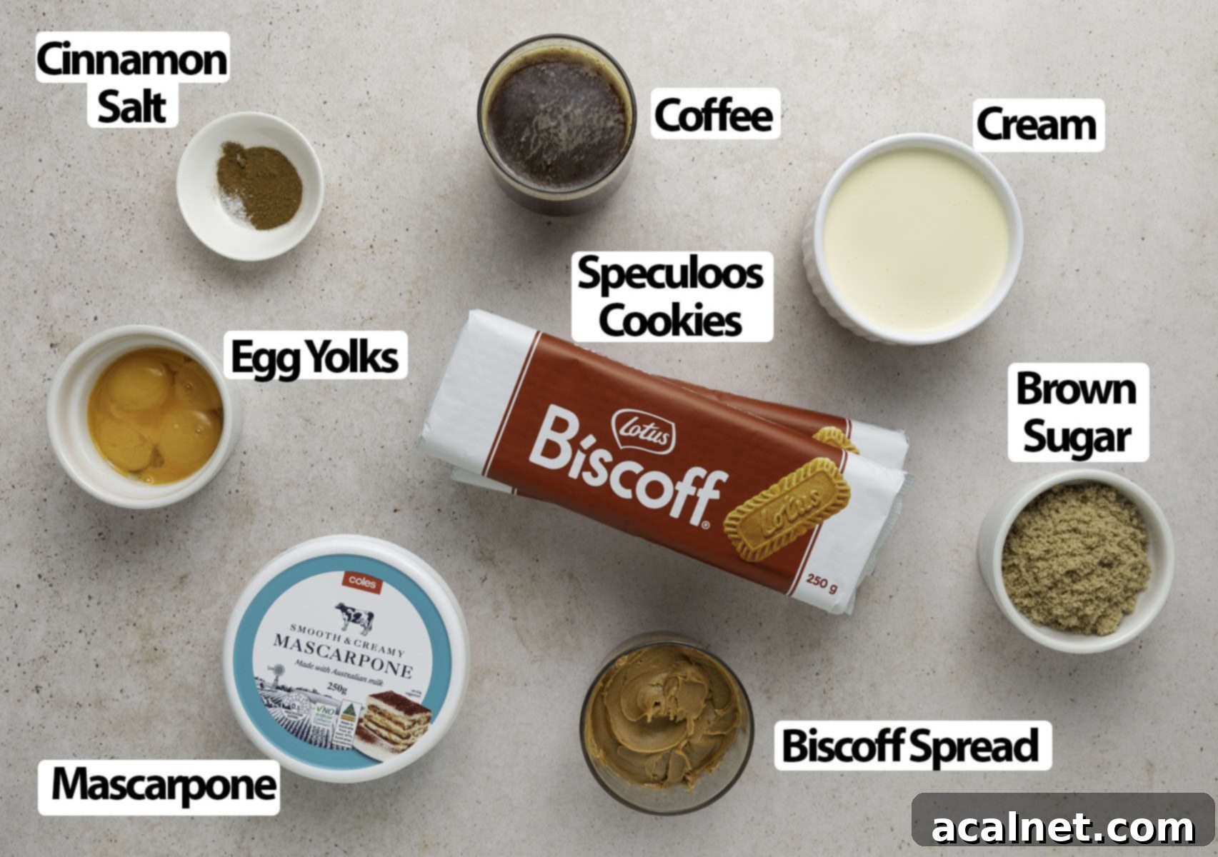 Ingredients laid out on a beige surface: speculoos cookies, coffee, eggs, biscoff spread, mascarpone cheese, heavy cream.