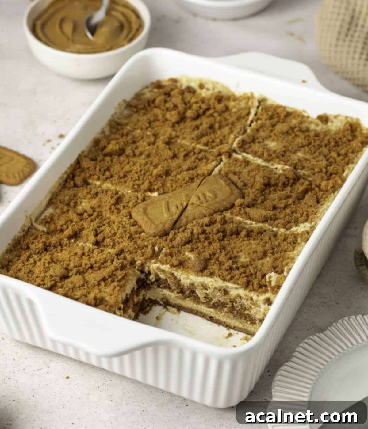 Tiramisu in a white ceramic dish with one portion taken out, showing its creamy texture.