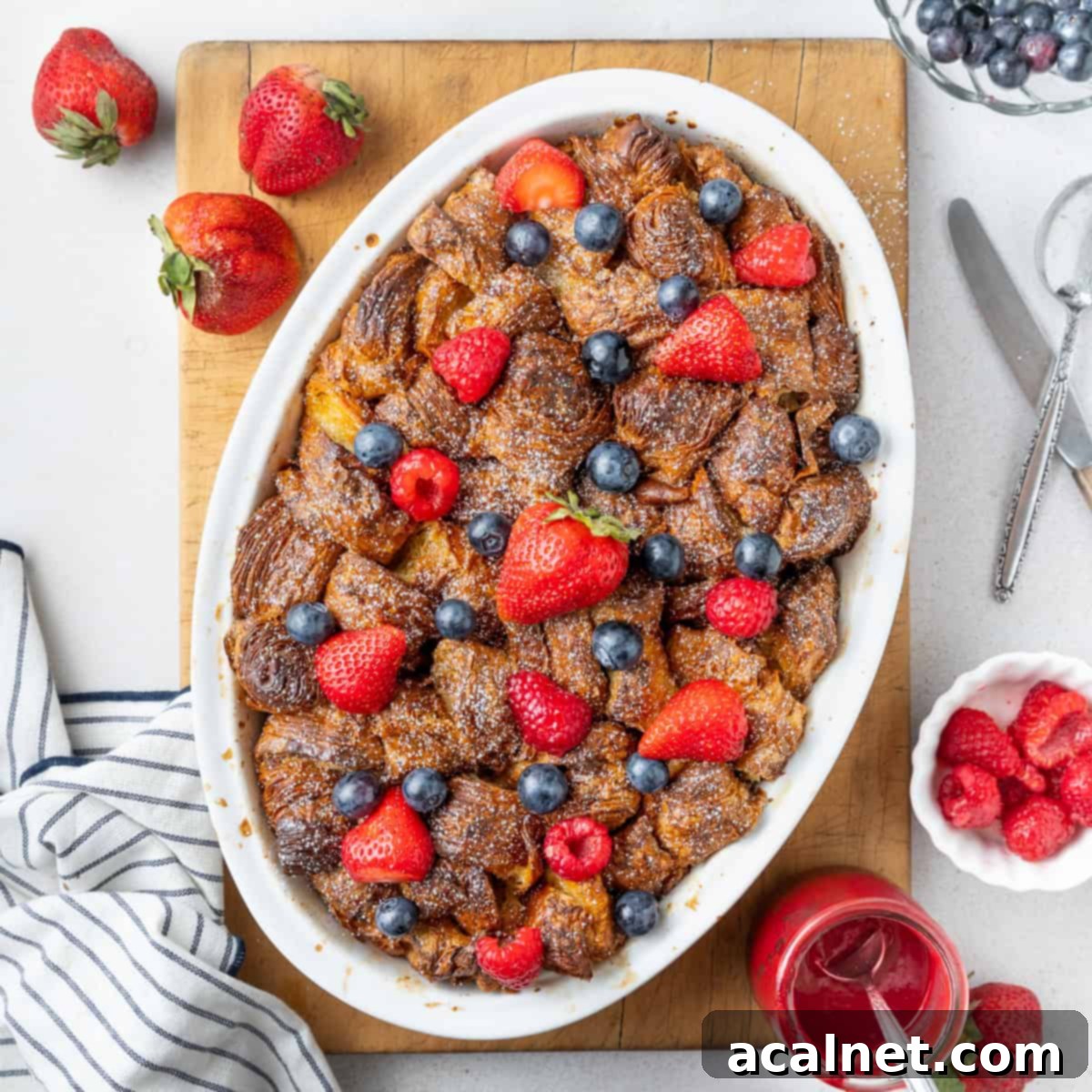 French toast baked in a white oval dish seen from above, placed on a rectangular cutting board and topped with fresh berries.