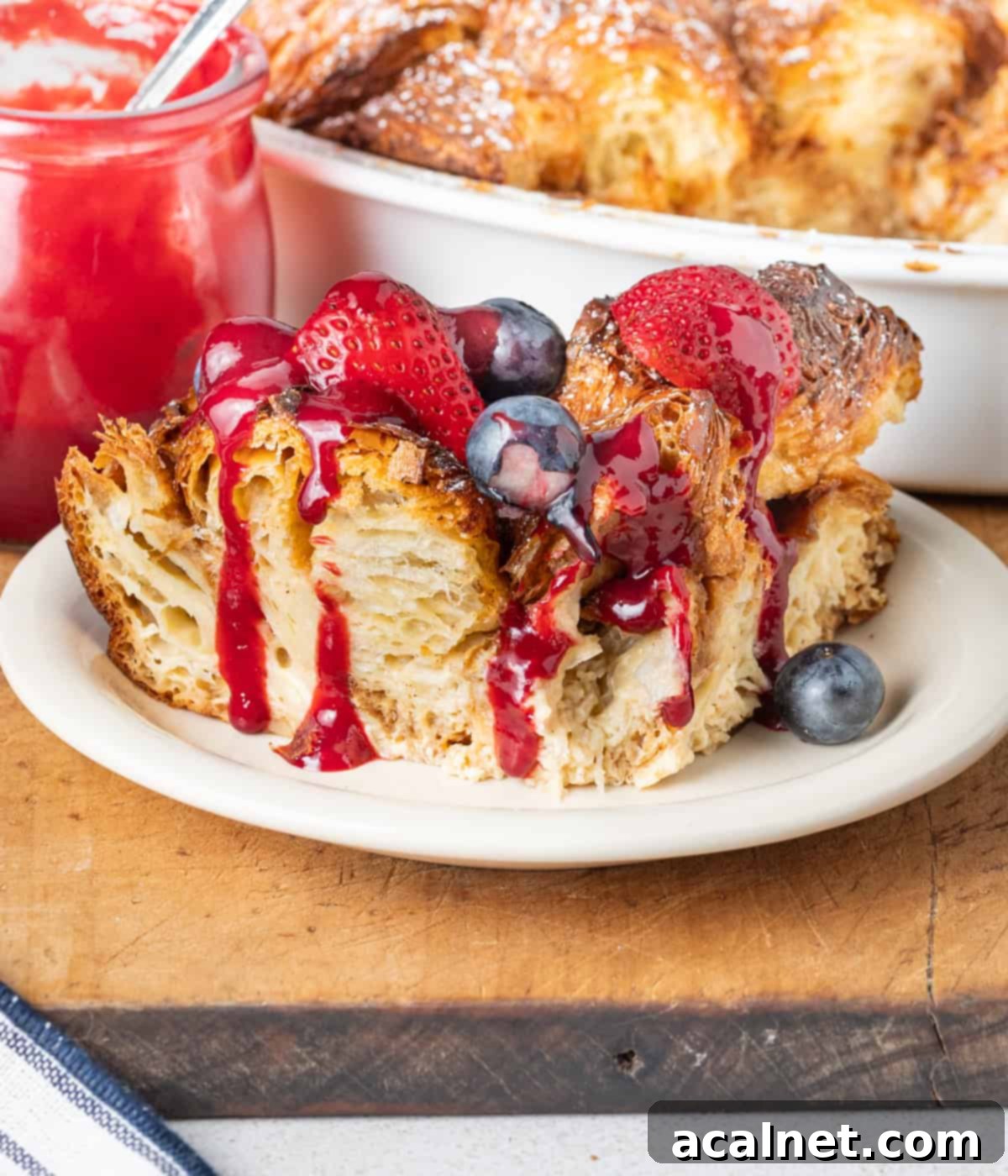 Slice of french toast on a small plate topped with fresh berries and raspberry coulis drizzle.