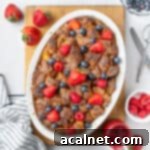 French toast baked in a white oval dish seen from above, placed on a rectangular cutting board and topped with fresh berries.