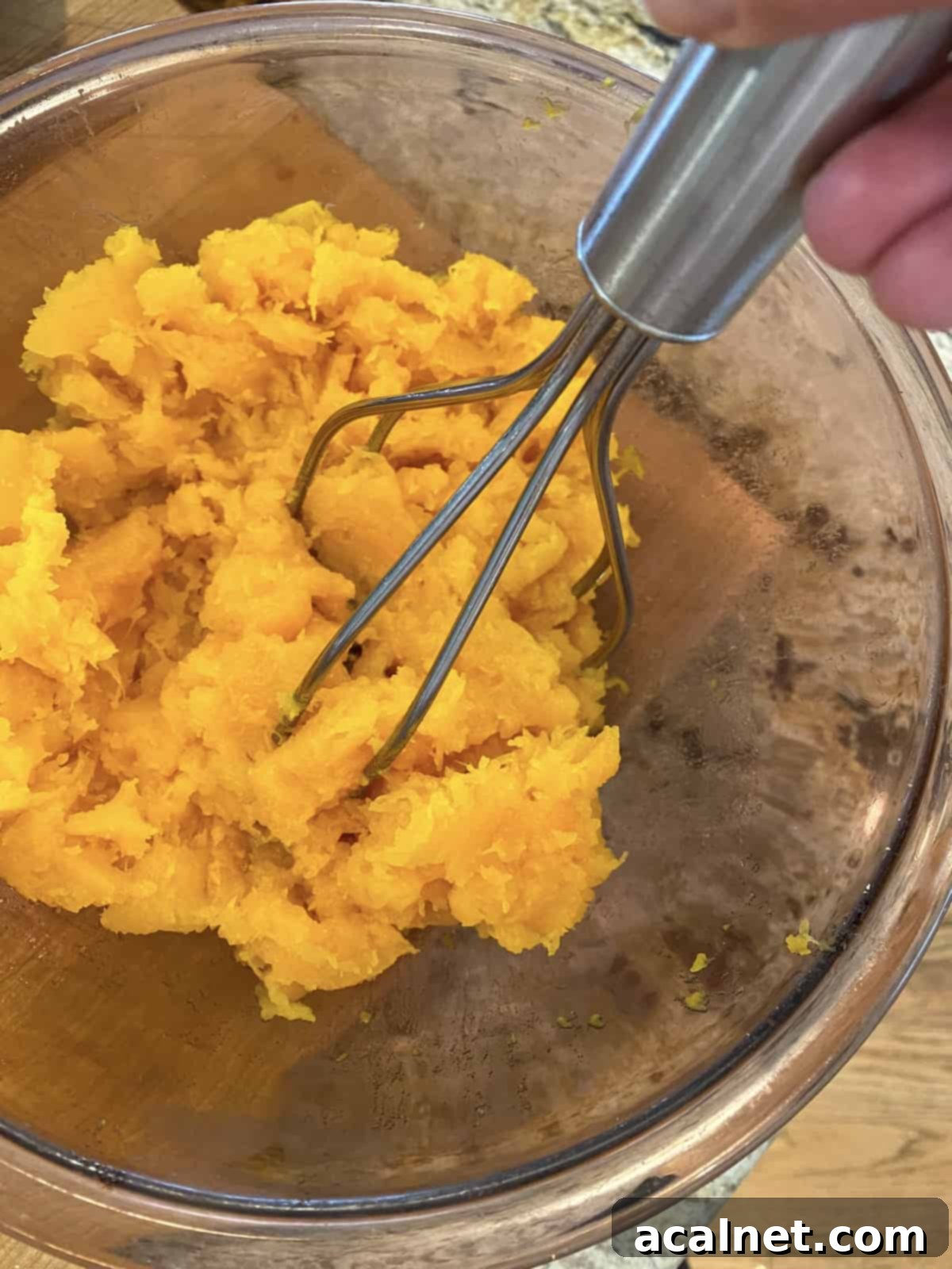 A potato masher actively mashing tender, cooked butternut squash in a medium-sized bowl to achieve a smooth texture.