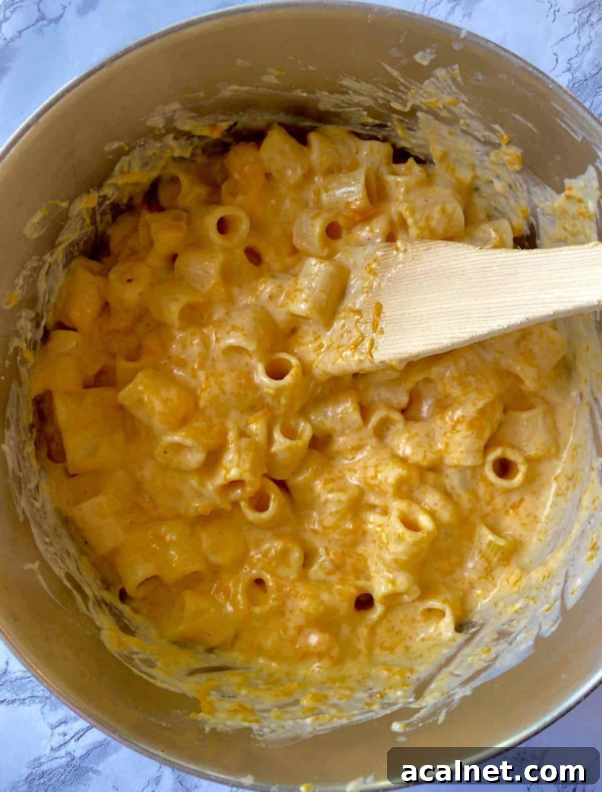 Cooked pasta being stirred into a rich, creamy cheese sauce with butternut squash in a saucepan using a wooden spoon, ensuring every piece is coated.