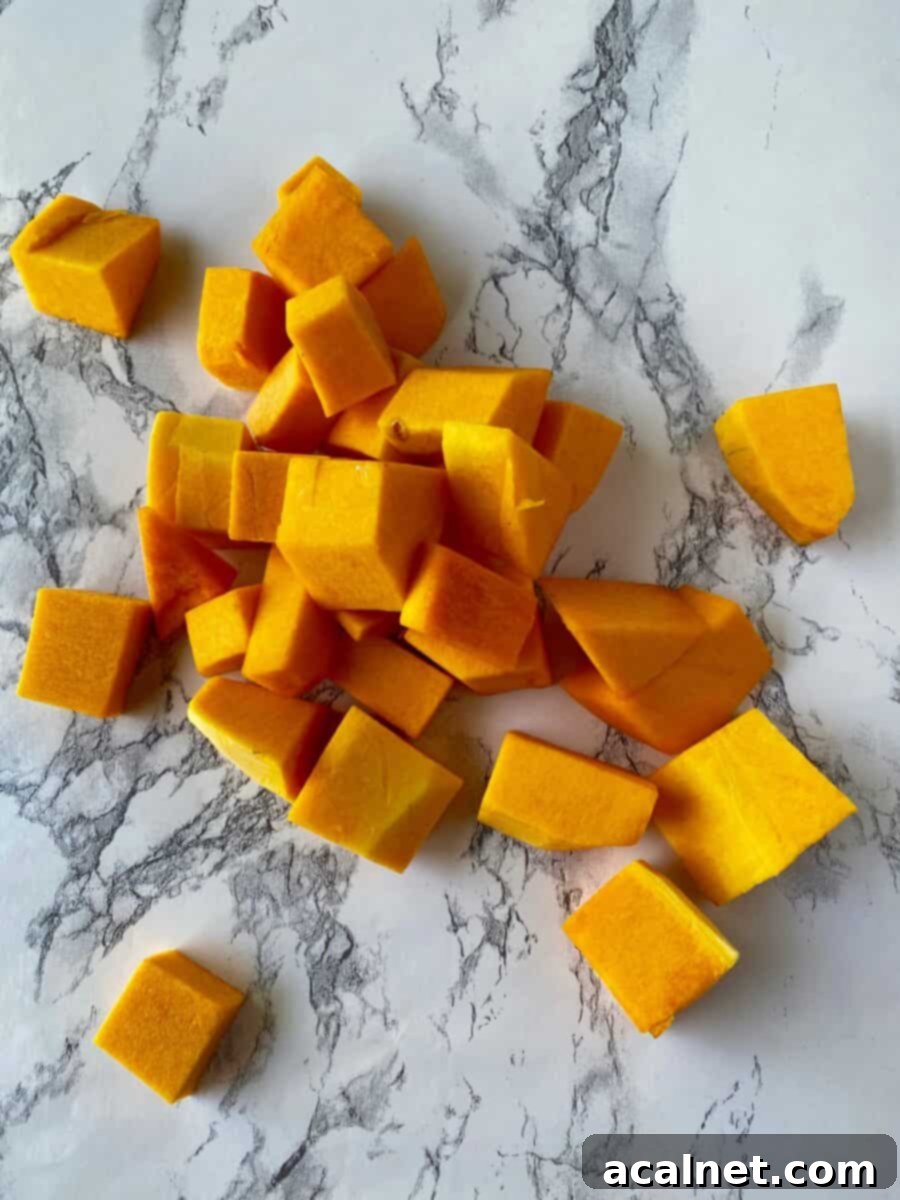 Freshly diced butternut squash cubes scattered on a clean white marble countertop, ready for preparation.