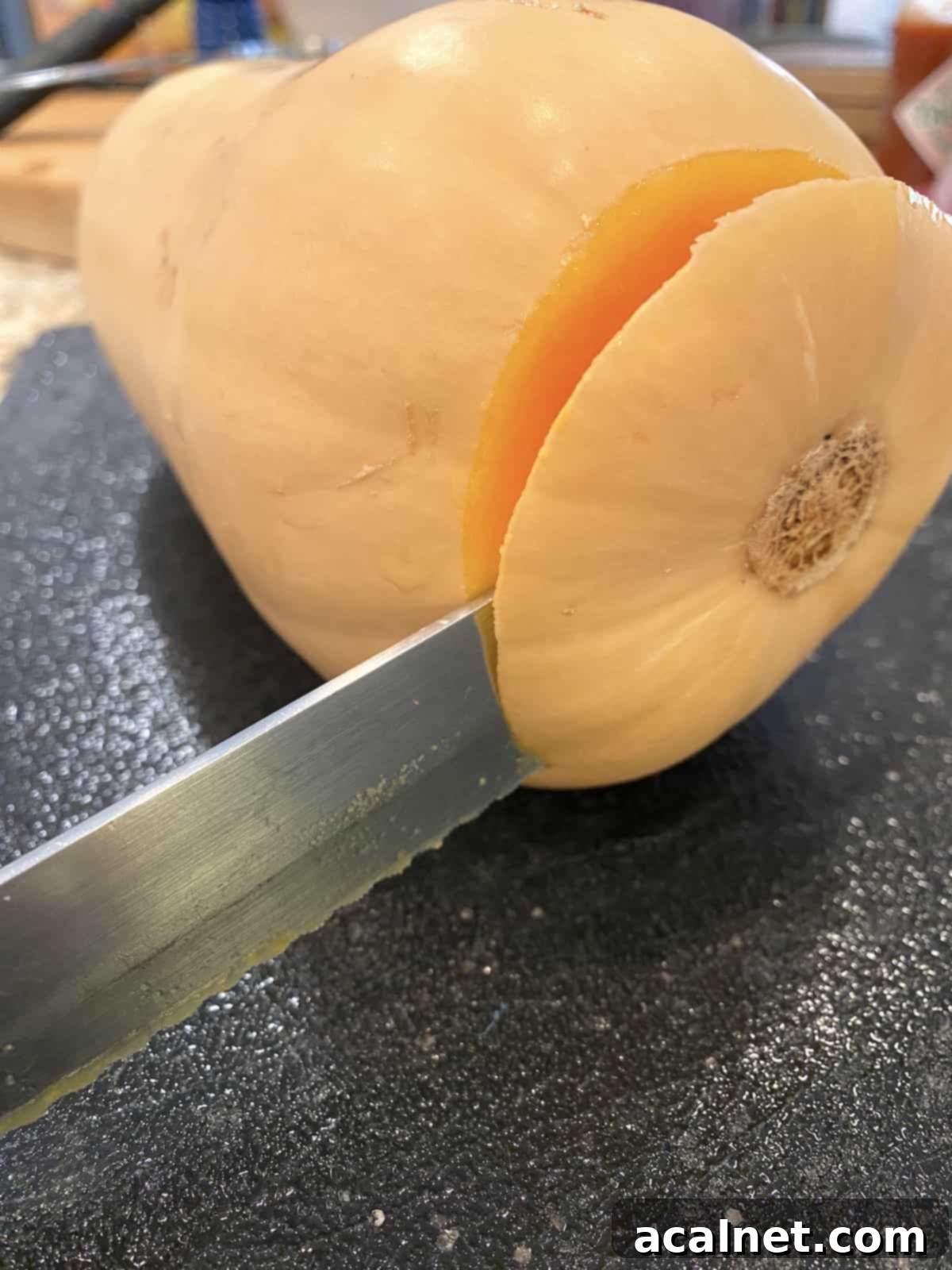 A kitchen knife precisely slicing off the tough end of a raw butternut squash on a cutting board.