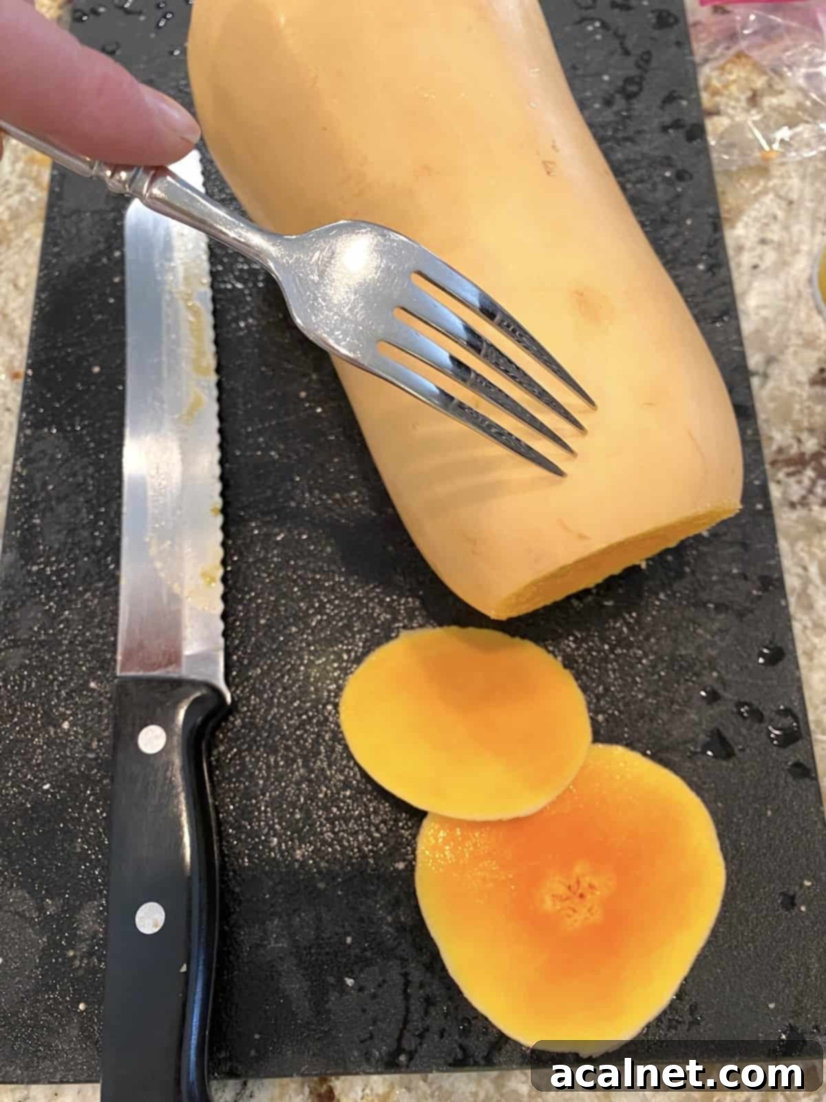 A fork piercing small holes into the skin of an uncooked butternut squash, with its sliced ends resting beside it on a cutting board.