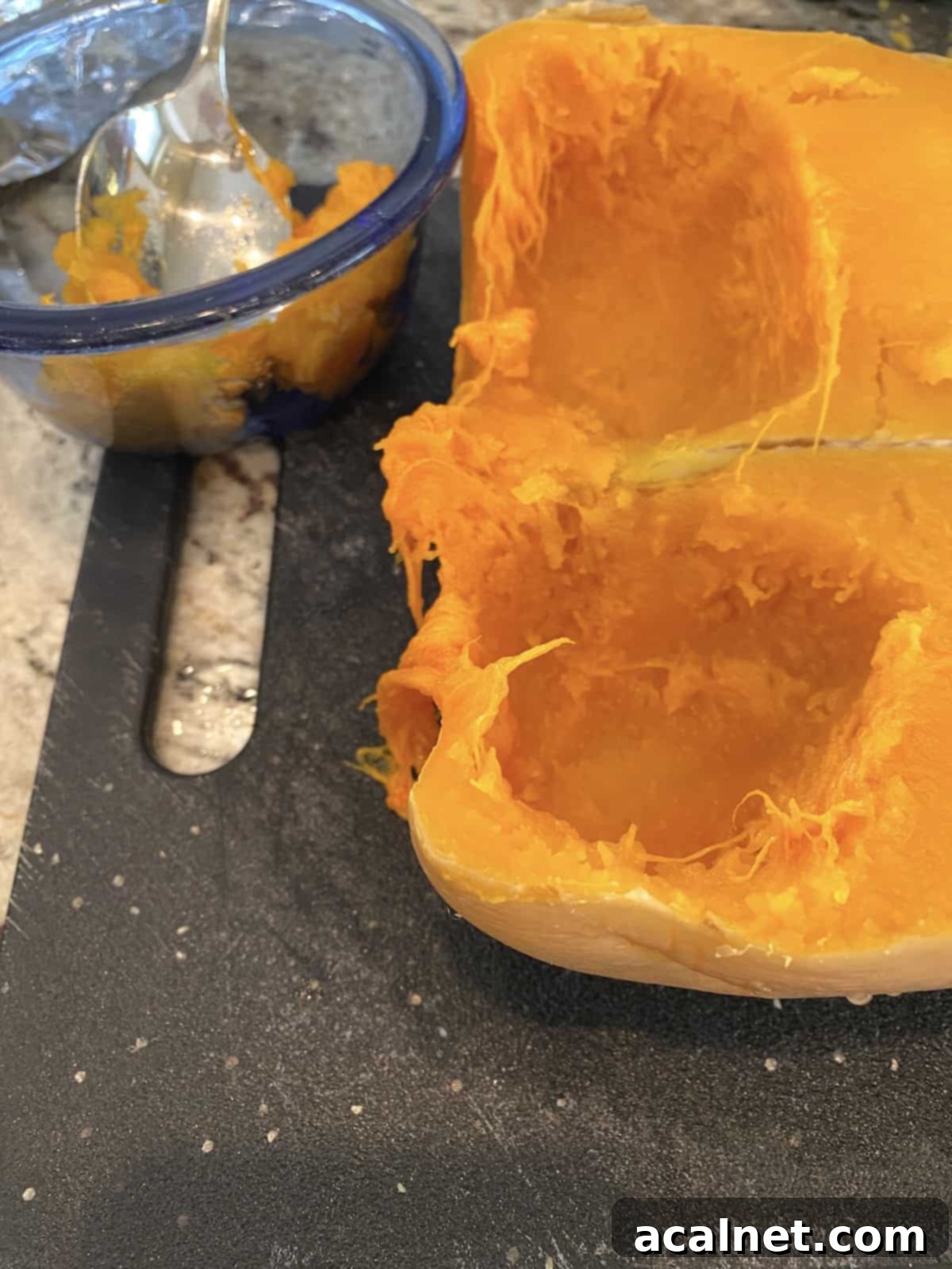 Two halves of a perfectly cooked butternut squash, with seeds scooped out, displayed on a cutting board next to a small bowl.