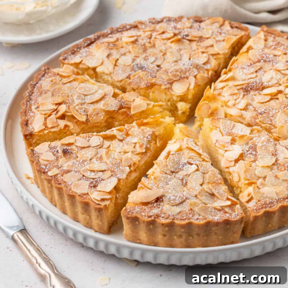 Sliced almond tart on a white plate, showcasing its layers of crust and filling.
