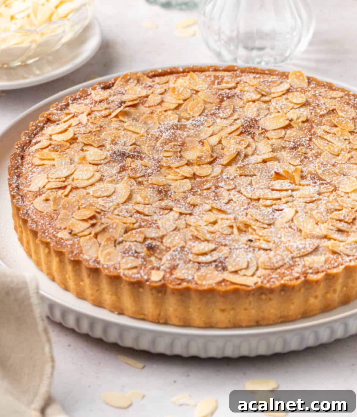 Side view of the almond tart placed on a large white plate, highlighting its golden crust and richly textured filling.
