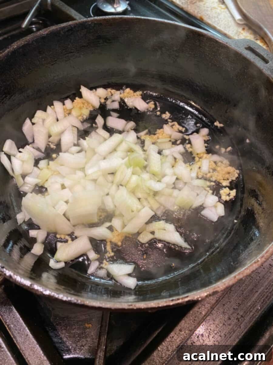Onions and garlic sautéing in a cast iron skillet on the stove, creating a fragrant base for the chicken.
