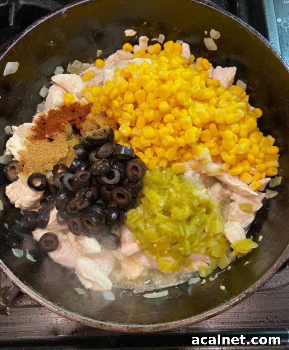 Olives, green chilies, corn, spices and chicken cooking together in a cast iron skillet, creating a rich taco filling.