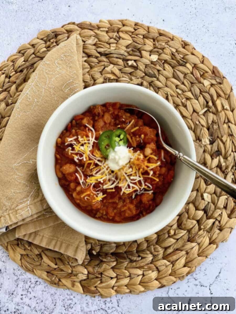 Hearty Idaho Chili 9 A beautifully set bowl of Idaho Chili, richly colored and garnished, placed on a striped placemat with a crisp napkin to the side, and a spoon resting in the chili, ready for the first satisfying bite.