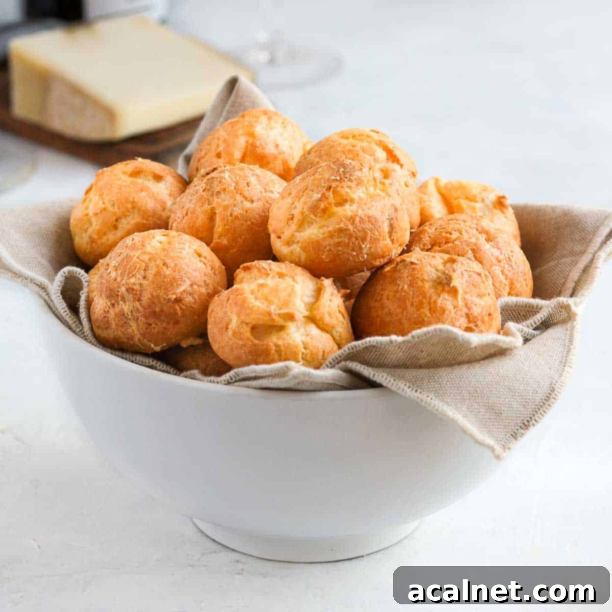 Cheese puffs in a white bowl over a beige napkin.