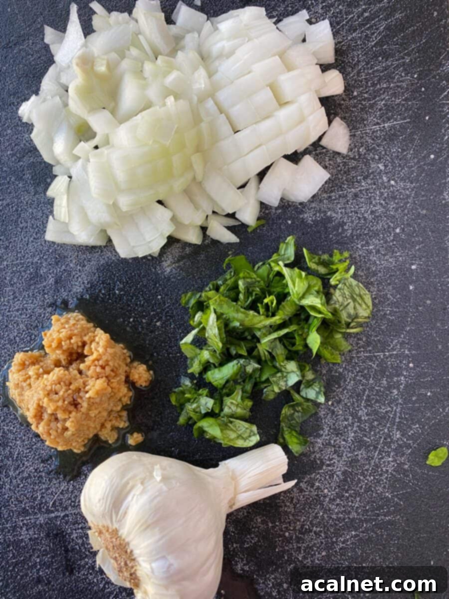 Ultimate Cheesy Ziti Bake 3 A wooden cutting board with finely chopped yellow onion, minced garlic cloves, and fresh green basil leaves, ready for sauce preparation.