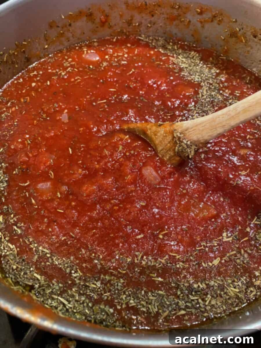 Ultimate Cheesy Ziti Bake 5 A large stock pot on a stove burner, filled with vibrant red marinara sauce, simmering gently with Italian seasoning sprinkled on top.