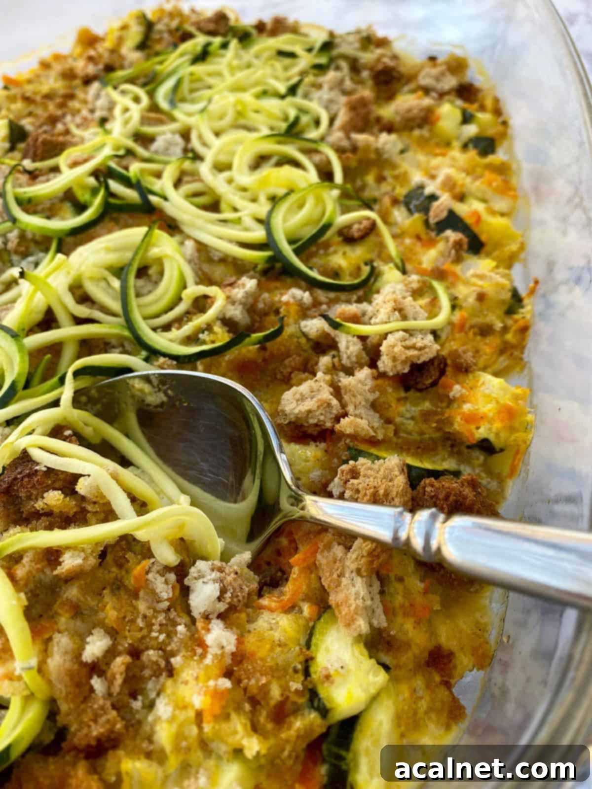 Baking dish with zucchini casserole and a serving spoon.