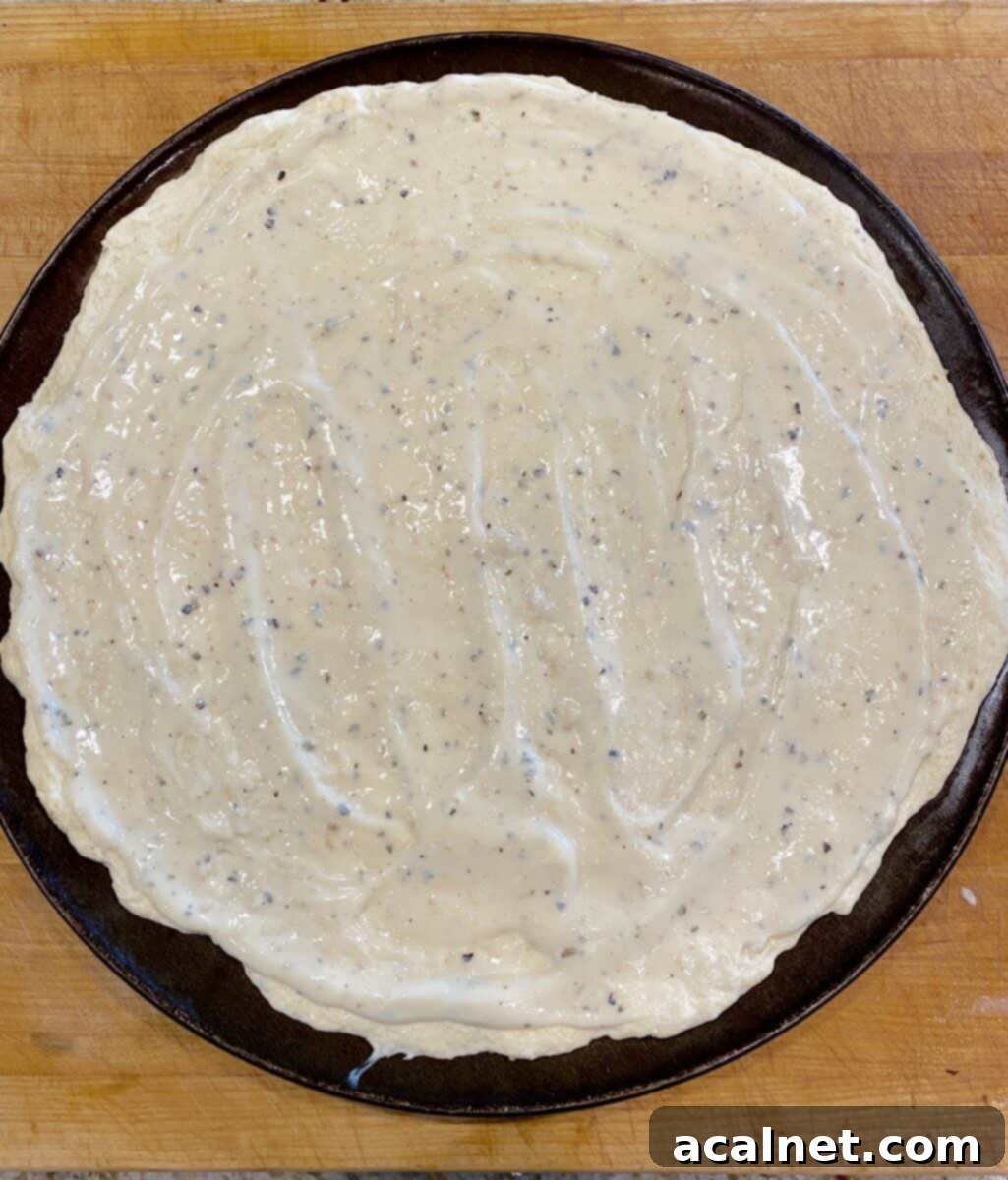 White pizza sauce on a large pizza crust in a pan.