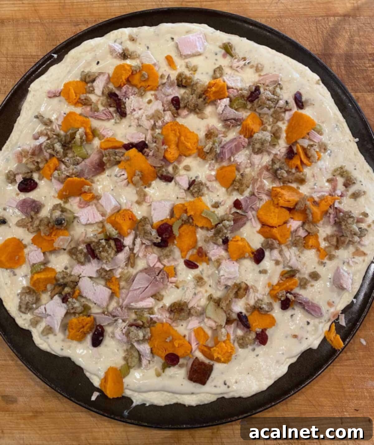 Leftover turkey, sweet potatoes and stuffing spread out on white pizza sauce.