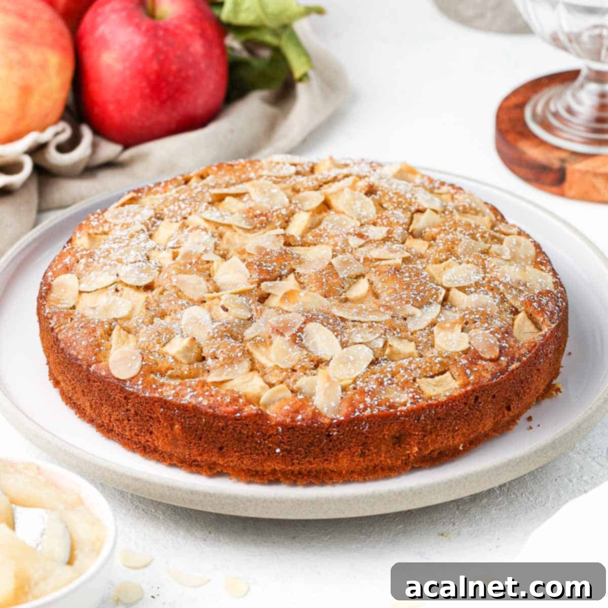 Cake on a large white serving plate surrounded by red apples.