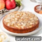 Cake on a large white serving plate surrounded by red apples.