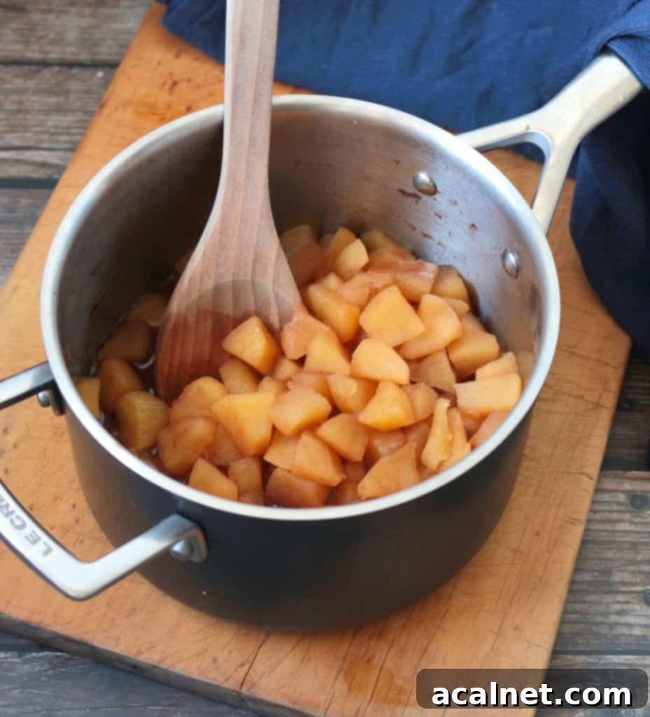 Cut apples simmering in a metal pot, cooking down into a soft mixture.