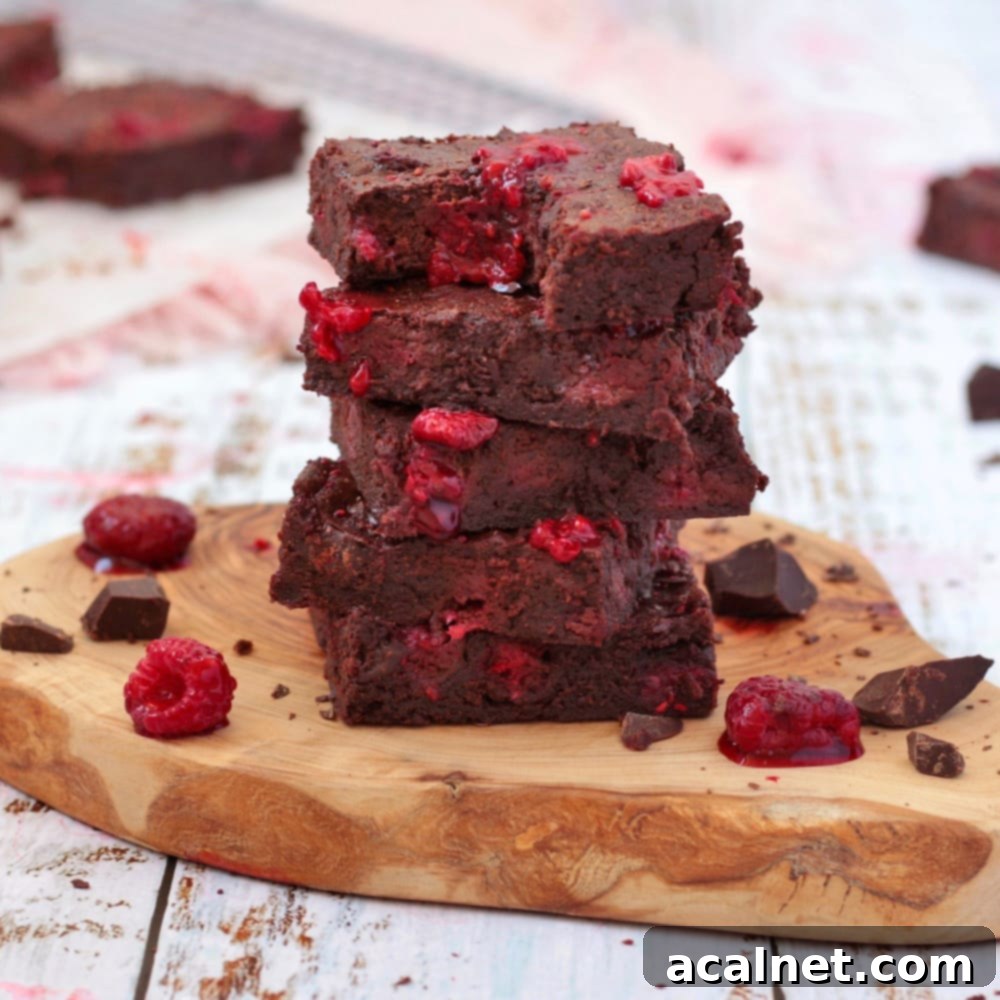 Stack of Raspberry Brownies on a wooden board, showcasing their fudgy texture and raspberry pieces.