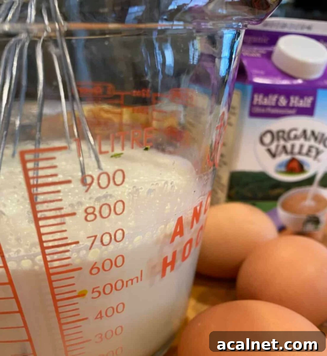 Half and half in a measuring cup with a whisk and three eggs.