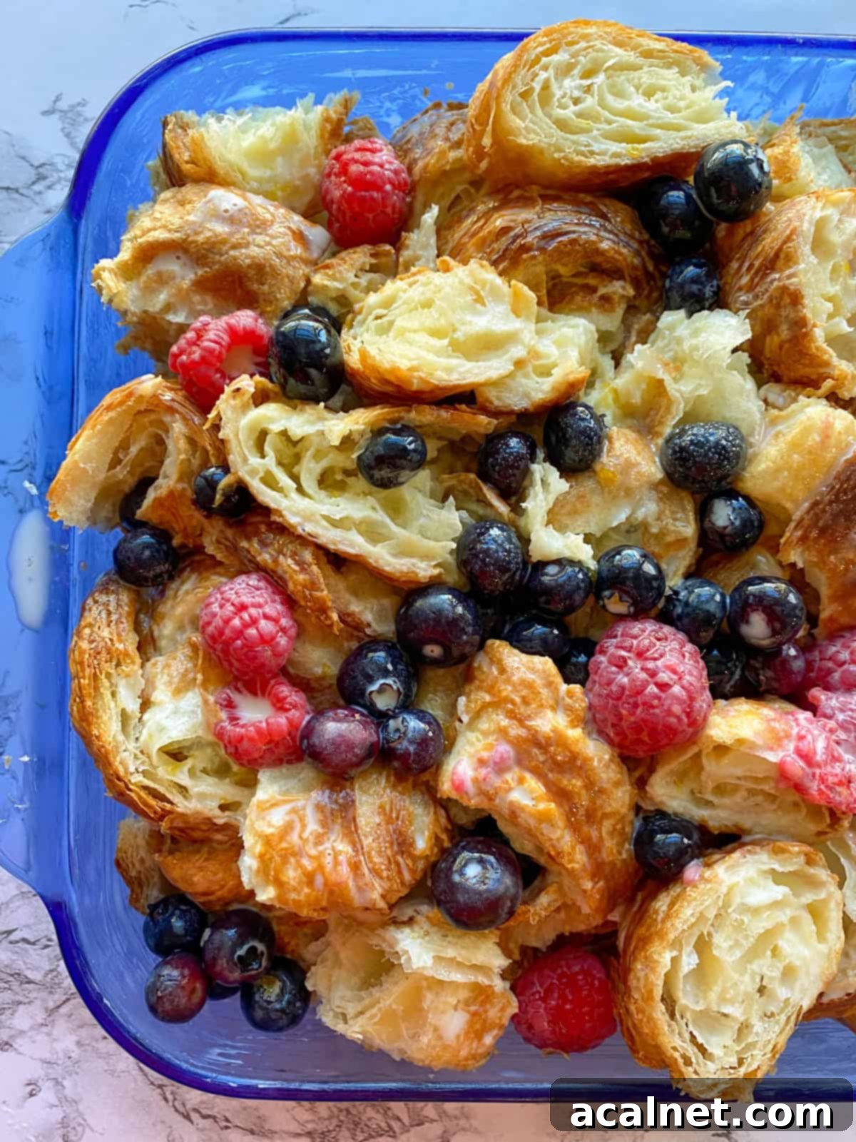 Croissant bread pudding with fruit in a baking dish, before baking.