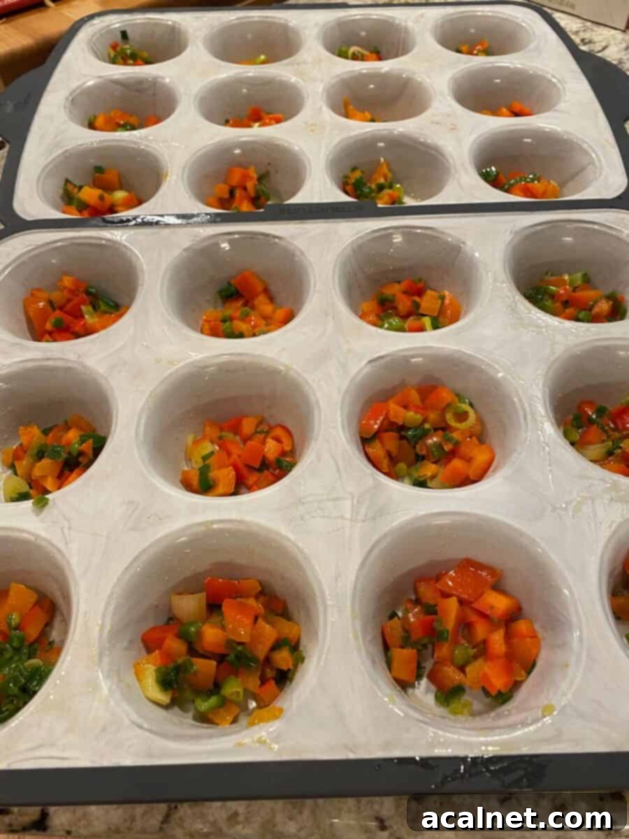 Twenty-four muffin cups filled with a colorful mixture of diced vegetables, ready for the egg mixture.