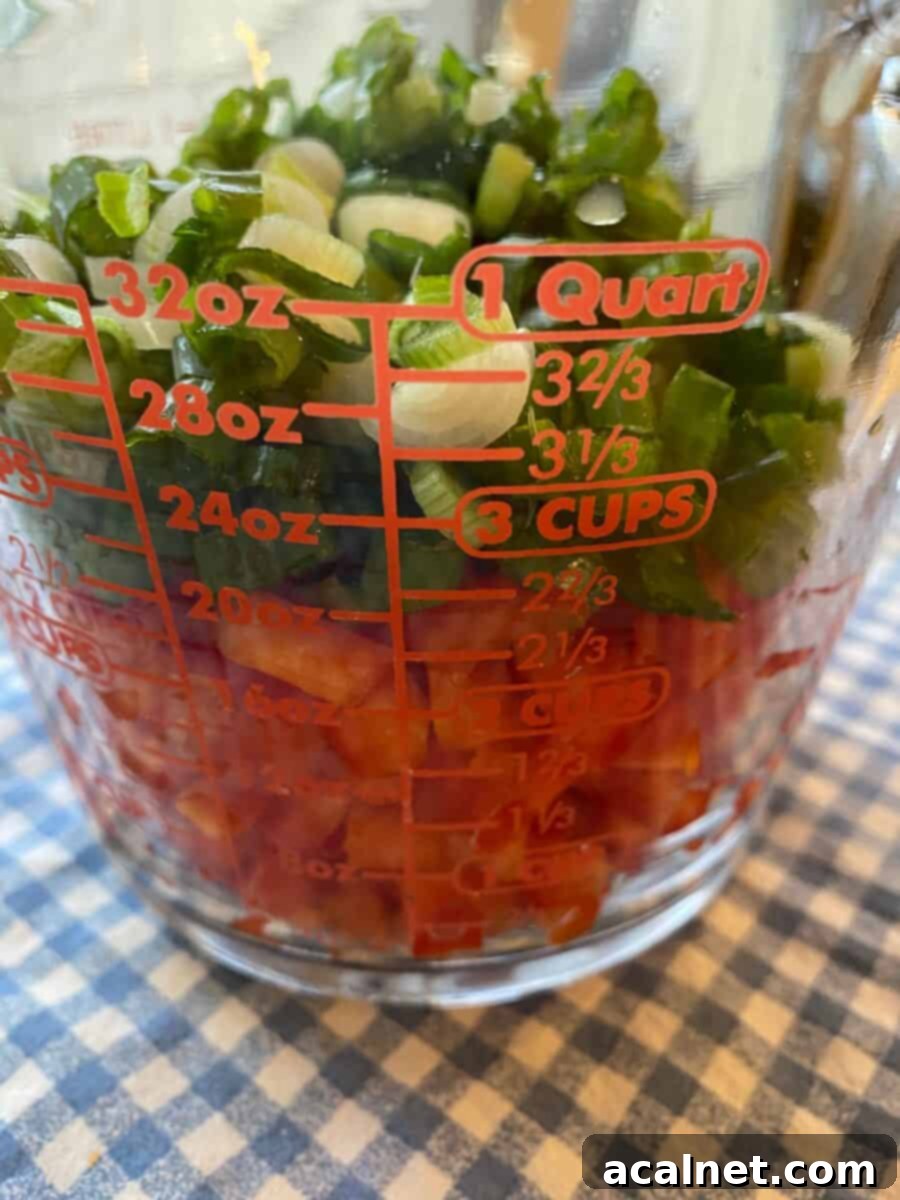 Measuring cup filled with a colorful mix of diced red peppers and chopped green onions.
