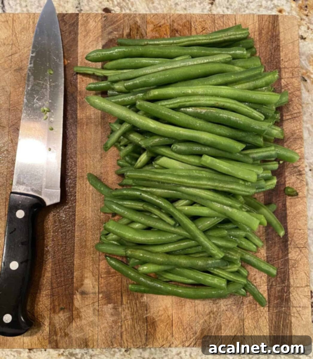 Fresh green beans arranged on a cutting board next to a sharp kitchen knife, ready for trimming.
