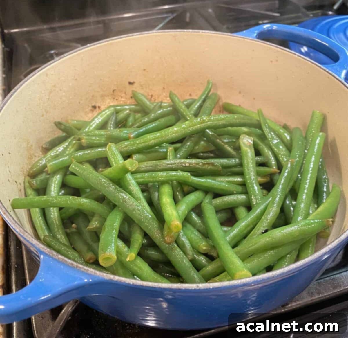 Fresh green beans being sautéed in a skillet on the stovetop, alongside minced garlic and olive oil.