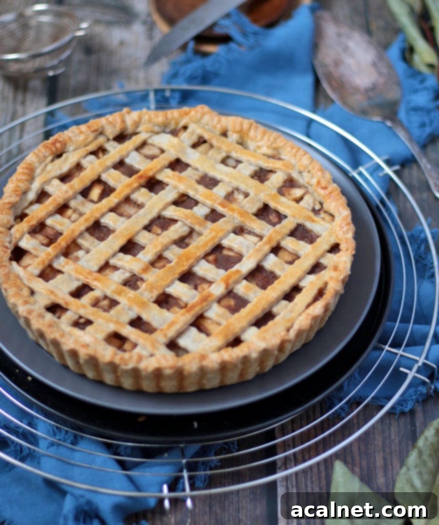 Orchard Fresh Pear Pie 3 A freshly baked pear pie on a grey plate, resting on a round cooling rack, showcasing its beautiful golden-brown crust.