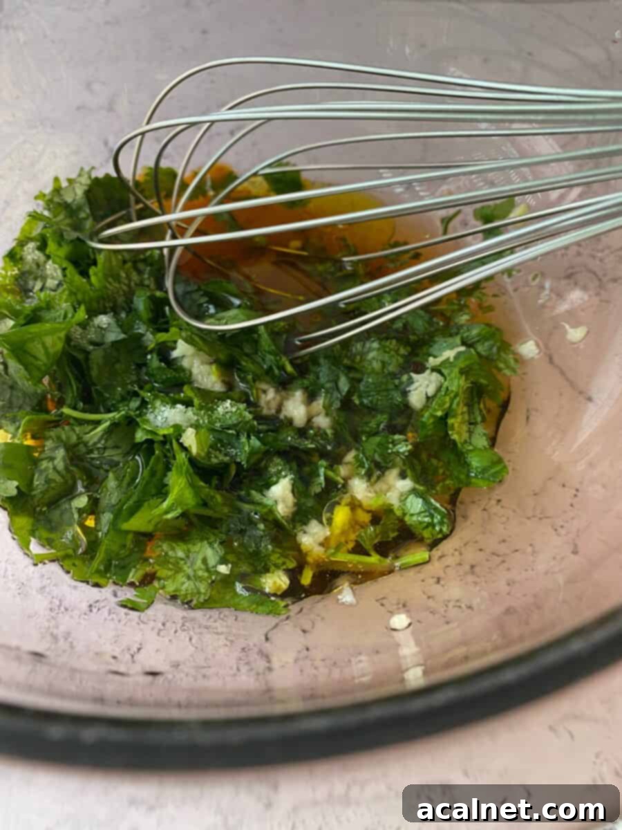 Ingredients for the vinaigrette, including fresh cilantro, red wine vinegar, and olive oil, in a bowl with a whisk.