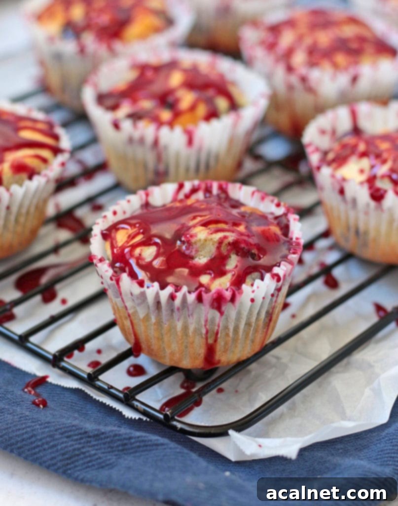 Baked lemon blueberry muffins, still warm on a cooling rack, drizzled generously with the vibrant Lemon Blueberry Glaze.