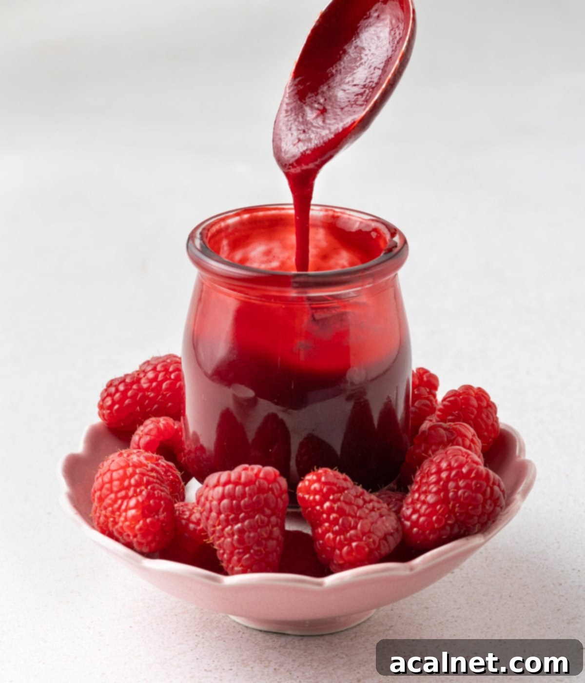 Effortless Raspberry Coulis 4 Coulis dripping from a large spoon inside a small jar.