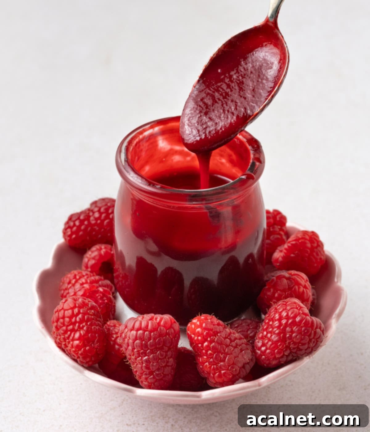 Effortless Raspberry Coulis 7 Raspberry sauce on a spoon, dripping inside a jar.